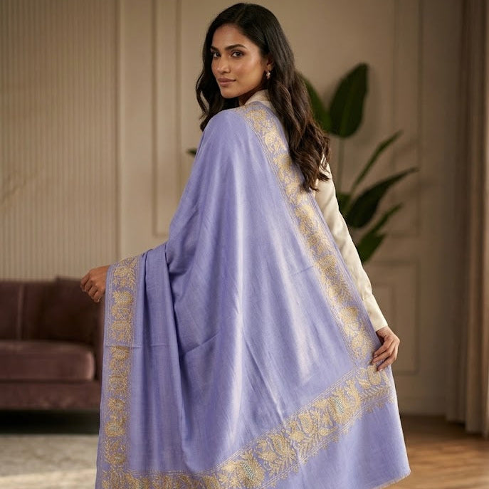A woman wearing a lavender purple shawl with gold embroidered borders, standing in a warm-toned indoor room.