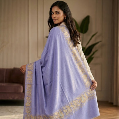 A woman wearing a lavender purple shawl with gold embroidered borders, standing in a warm-toned indoor room.