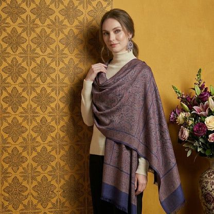 Woman wearing a patterned shawl against a decorative wall with a vase of flowers.