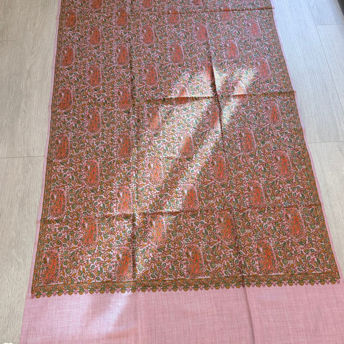 A rectangular pink and brown patterned fabric, likely a dupatta or scarf, laid flat on a light wood floor. The fabric features a central brown field with a repeating orange and beige paisley pattern, bordered by solid pink sections at the top and bottom.