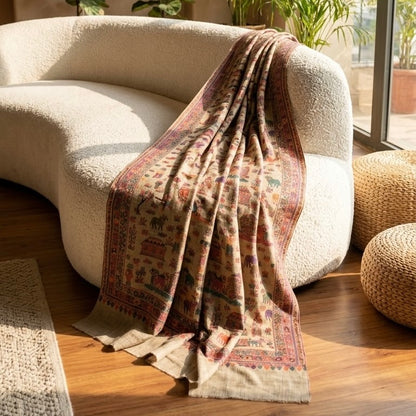A beige wool shawl with a colorful traditional Indian-style print draped over a cream-colored curved sofa in a sunlit room.
