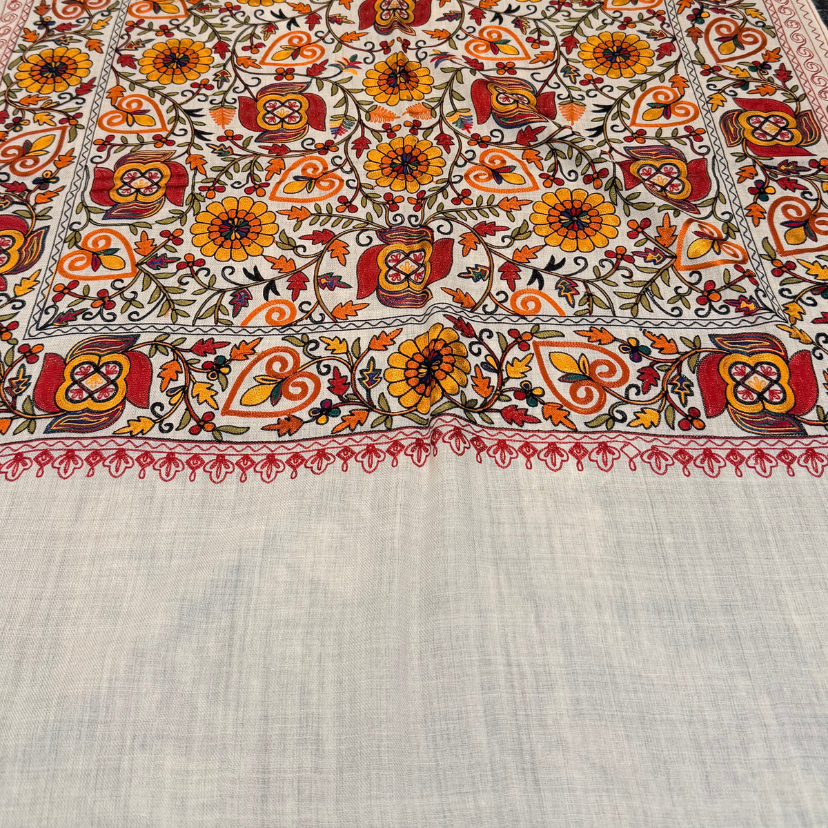 A large rectangular woven textile laid flat on a dark countertop, featuring an ornate multicolor floral and geometric pattern with a wide plain off-white lower section and fringe along one edge.