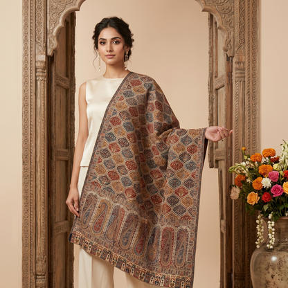 Woman holding a patterned shawl in front of an ornate door with a vase of flowers.
