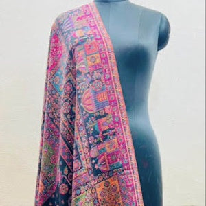 A multicolor patterned shawl draped over a dark gray mannequin torso against a light beige wall.