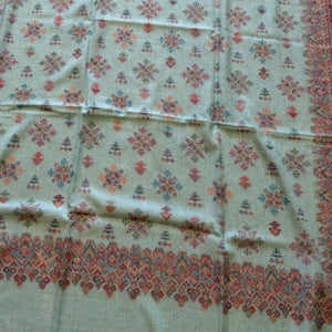 A light sage green fabric with a repeating red and orange floral pattern and a decorative border along the bottom edge.