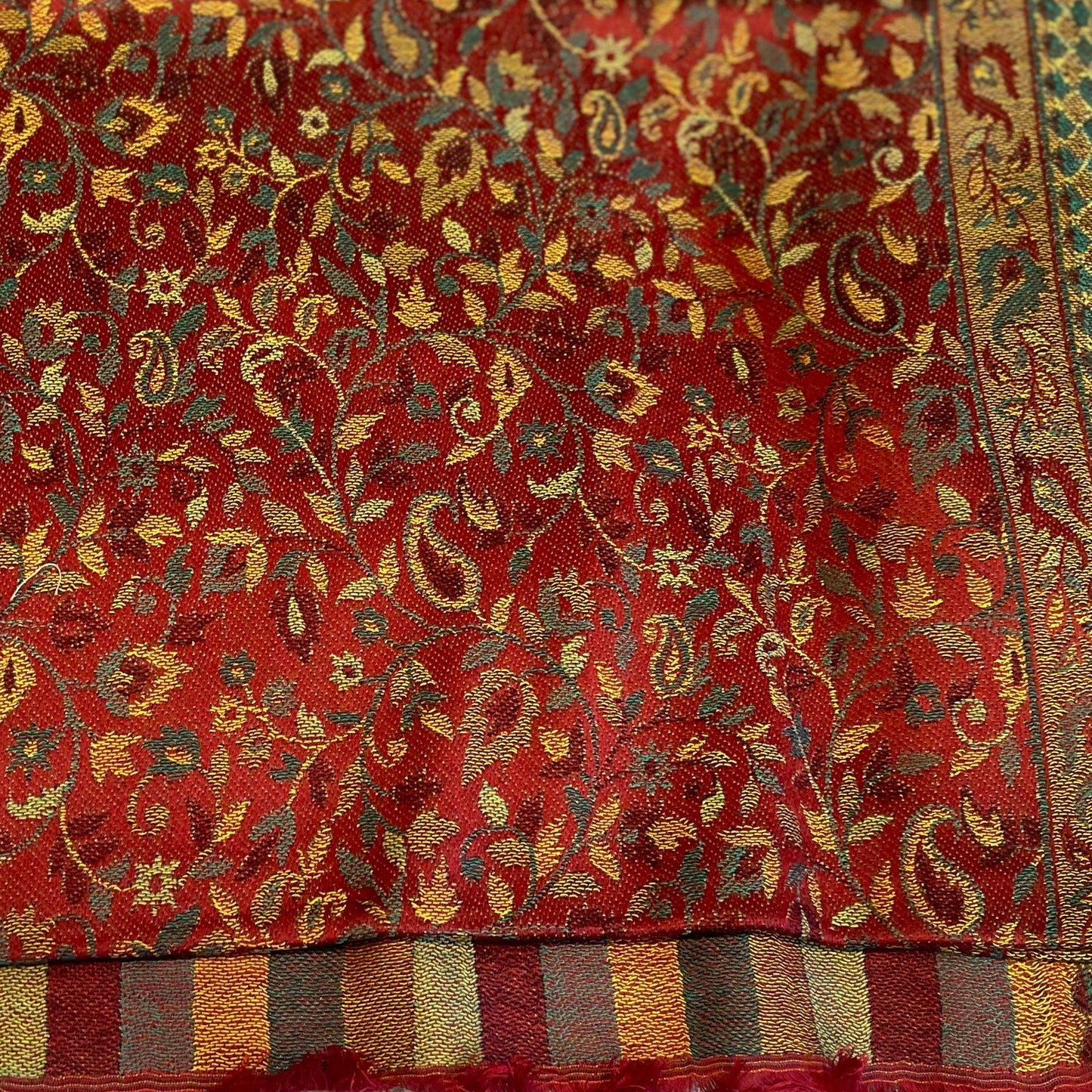 Close-up of a red fabric with intricate gold and green floral patterns