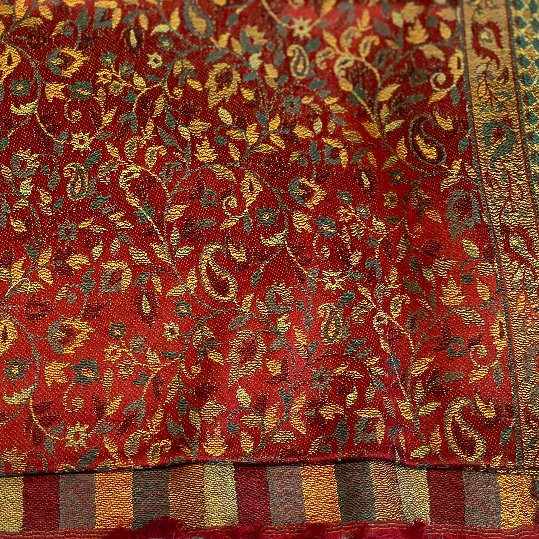 Close-up of a red fabric with intricate gold and green floral patterns