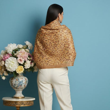Woman wearing a patterned coat standing in front of a blue wall with a decorative table and flowers.