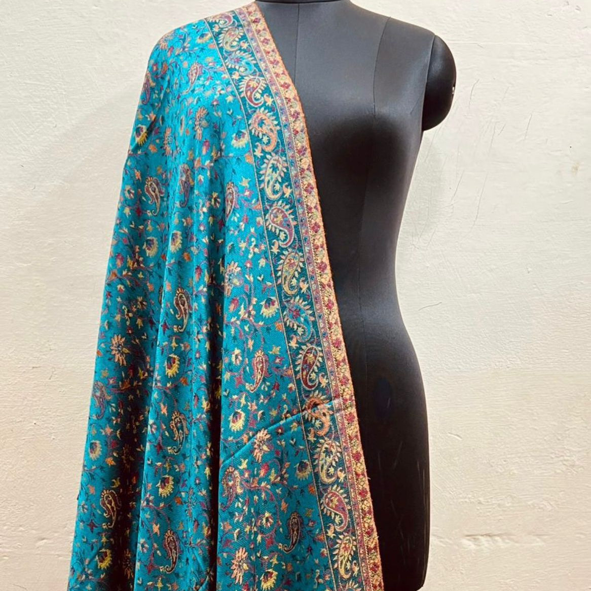 Azure blue faux Pashmina stole with intricate patterns draped over a black mannequin against a beige background