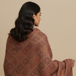 Woman draped in a pink patterned shawl against a beige background