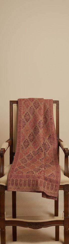 Patterned pink shawl draped over a wooden chair against a beige wall.