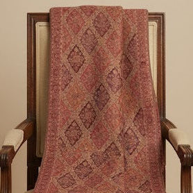 Patterned pink shawl draped over a wooden chair against a beige wall.
