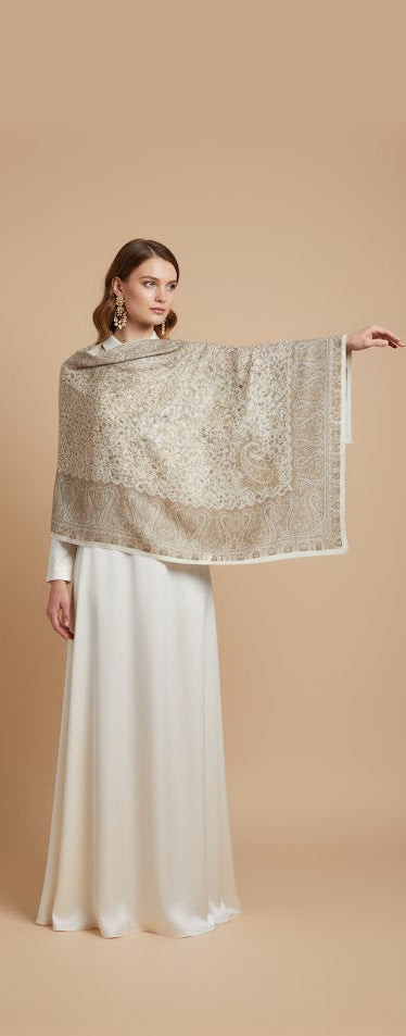 Woman wearing a gold shawl over a white dress on a beige background