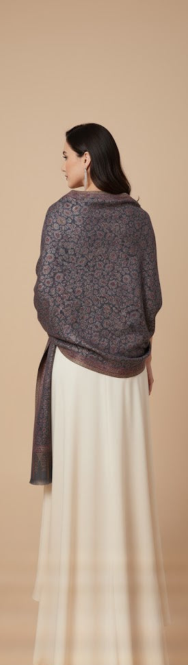 Woman wearing a dark gray patterned shawl over a white dress against a beige background