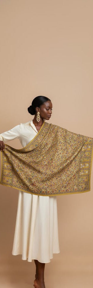 Woman holding a patterned gold scarf against a beige background