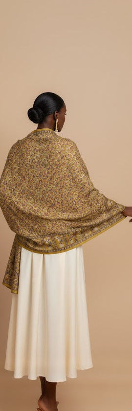 Woman wearing a gold shawl over a white dress against a beige background