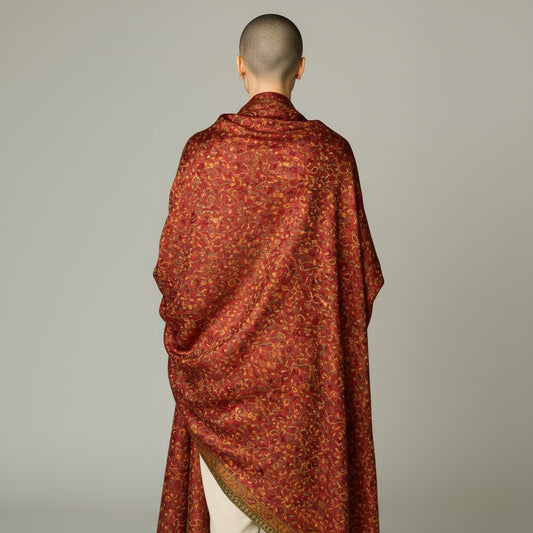 Person draped in a red patterned shawl against a plain background