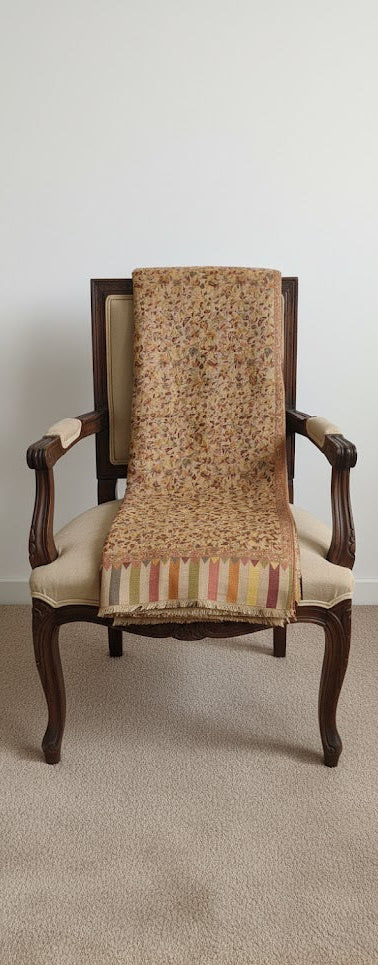 Wooden armchair with a patterned shawl draped over it on a plain background