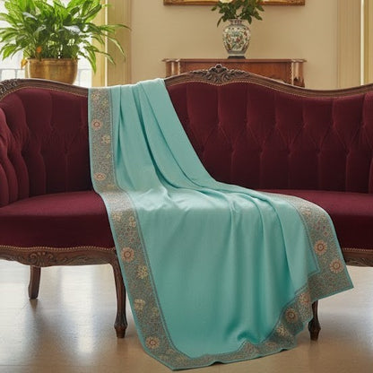 Turquoise blanket with floral patterns draped over a red sofa in a room with plants and a vase.