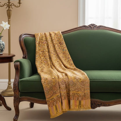 Gold patterned throw blanket draped over a green sofa in a room with a beige wall and a window.