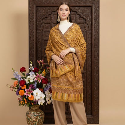 Woman in a patterned yellow outfit standing next to a decorative wooden panel and floral arrangement.