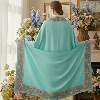 Woman holding a turquoise shawl with floral patterns in a room with flowers and decor.