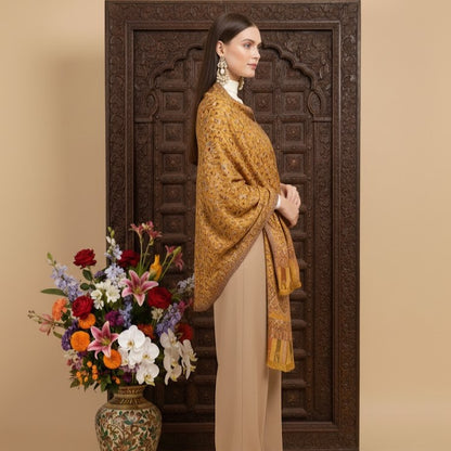 Woman wearing a mustard yellow shawl standing next to a floral arrangement in front of an ornate wooden door.