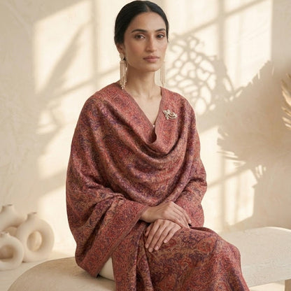 Woman wearing a patterned shawl sitting on a chair with a neutral background