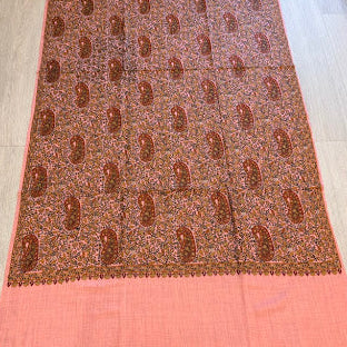 A pink and brown patterned scarf or sari laid flat on a light wood floor, featuring a central brown patterned section with paisley motifs and solid pink borders at the top and bottom.