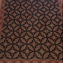 A rectangular area rug with an intricate geometric medallion pattern in dark brown, black, and beige, featuring a decorative border and fringe, shown in a mobile app mockup view.