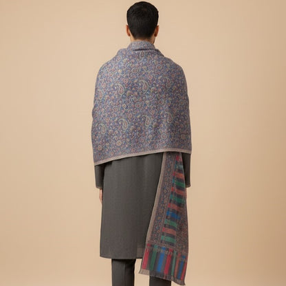 Person wearing a patterned shawl over a gray coat on a beige background