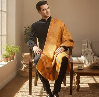 Man sitting in a chair wearing an orange patterned shawl in a cozy room.