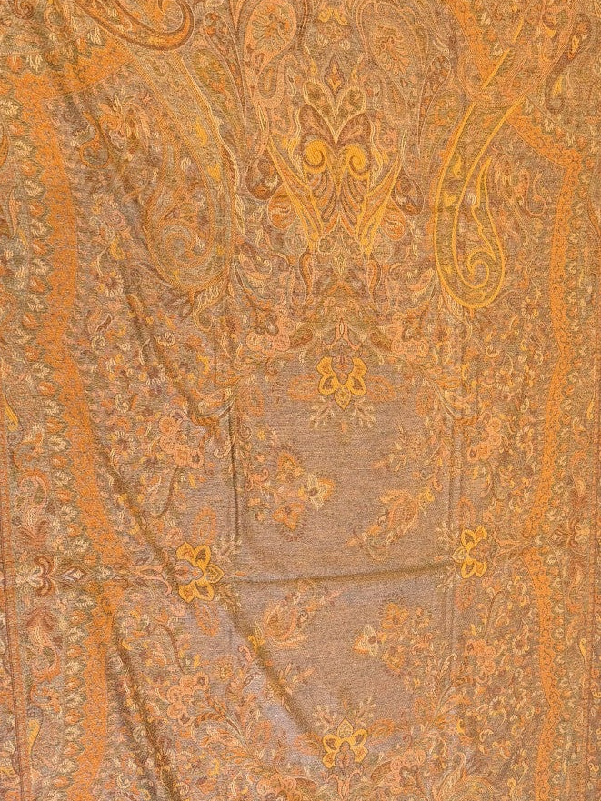 Decorative saffron gold yellow pure wool hand embroidered kani jamawar shawl with intricate patterns on a wall next to a modern gray sofa.