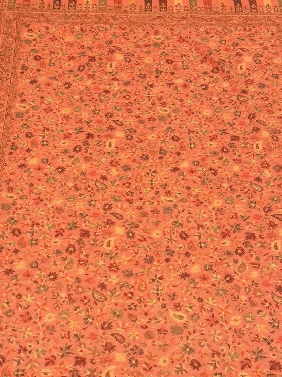 Decorative folded pink pure wool shawl with intricate patterns on a light wooden floor.