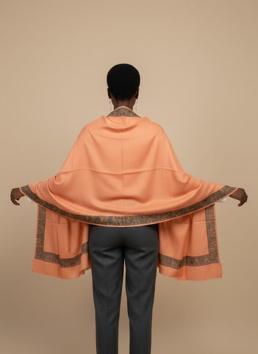 Person wearing a peach pashmina shawl  with intricate patterns on a beige background