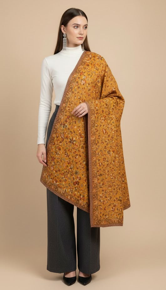 Woman wearing a patterned Yellow floral patterned kani design shawl  over a white top and black pants on a beige background
