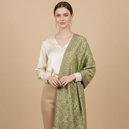 Woman wearing a sage green paisley patterned faux pashmina silk blend over a cream blouse and beige pants on a beige background