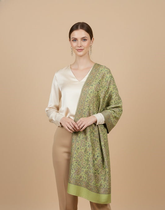 Woman wearing a sage green paisley patterned faux pashmina silk blend over a cream blouse and beige pants on a beige background