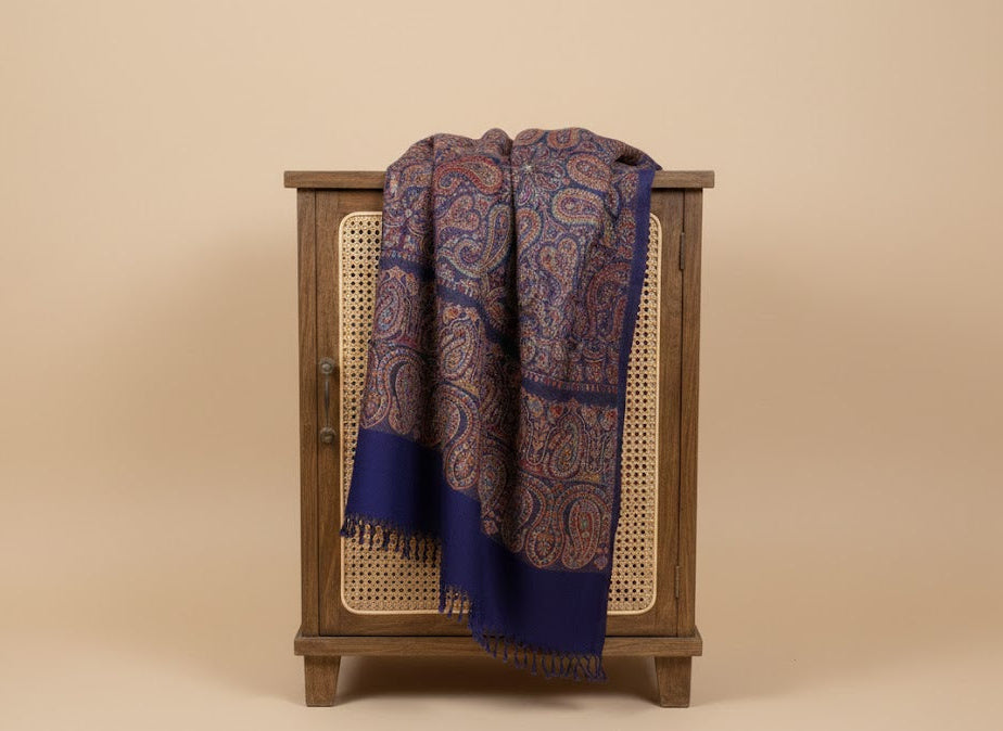 Wooden cabinet with a patterned blue silk wool blend, large patterned jamawar kani shawl with intricate paisley pattern draped over it on a beige background