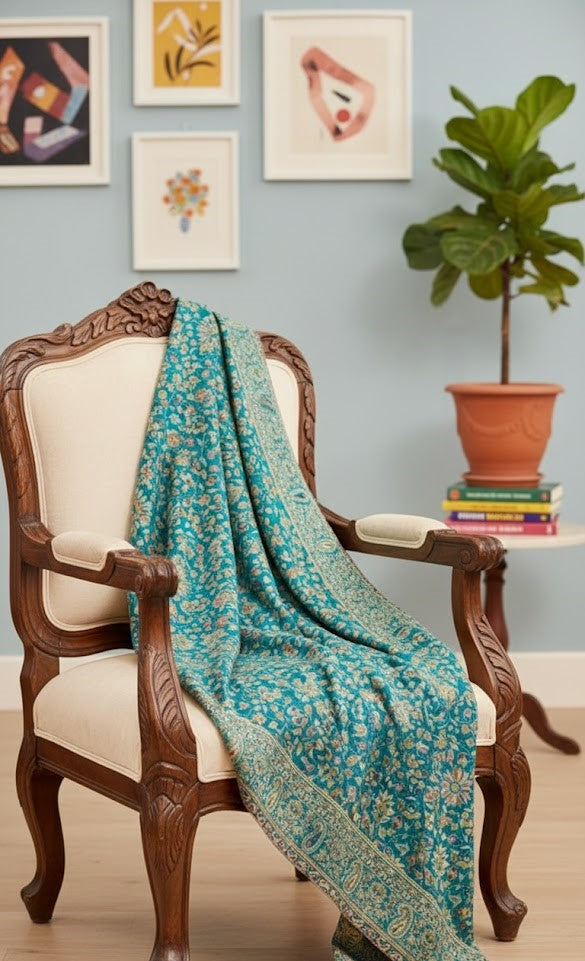 Teal floral shawl draped over a wooden chair with a plant and books in the background.