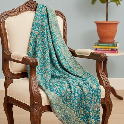 Teal floral shawl draped over a wooden chair with a plant and books in the background.