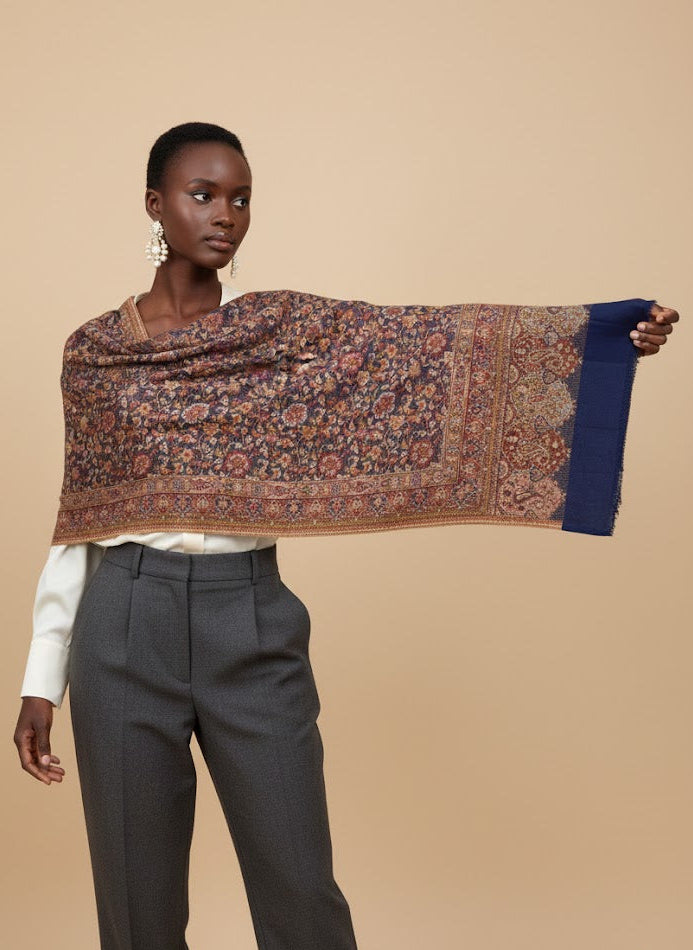 Woman holding a patterned deep indigo blue hand woven pure wool patterned jamawar kani shawl against a beige background