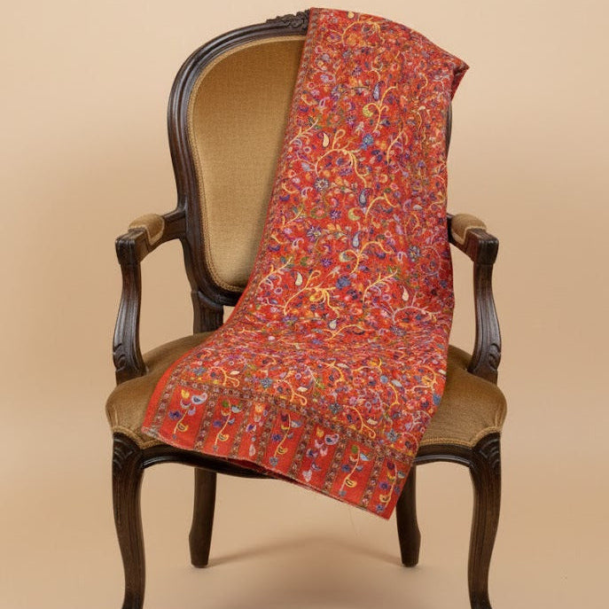 Decorative red paisley patterned kalamkari-inspired stole in faux pashmina draped over a wooden chair against a beige background