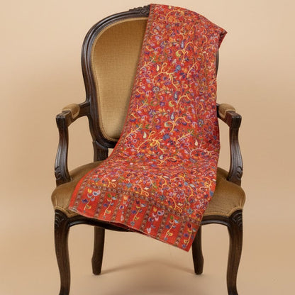 Decorative red paisley patterned kalamkari-inspired stole in faux pashmina draped over a wooden chair against a beige background