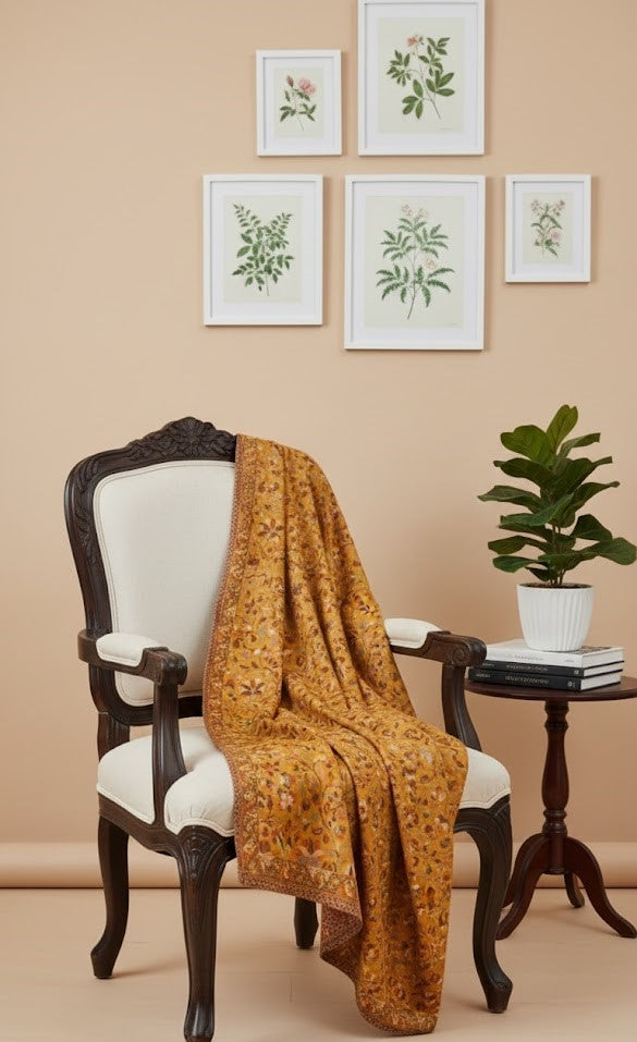 Brown floral Yellow floral patterned kani design shawl draped over a white chair with framed botanical prints on the wall.