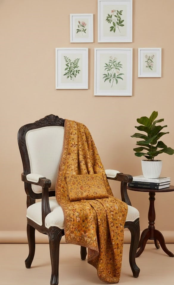 Yellow patterned kalamakari kani double beam stole in pure wool draped over a white chair with framed botanical prints on the wall.