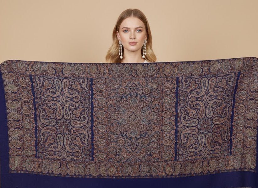 Woman holding a large patterned silk wool blend, jamawar kani shawl with intricate paisley pattern against a beige background