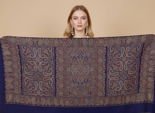Woman holding a large patterned silk wool blend, jamawar kani shawl with intricate paisley pattern against a beige background