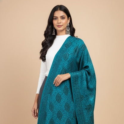 Female model wearing a blue patterned faux Pashmina stole over a white top and black pants on a beige background