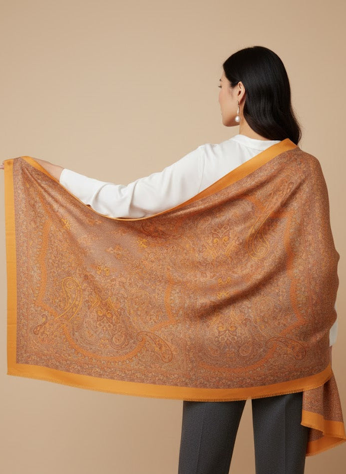 Woman wearing an saffron gold yellow pure wool hand embroidered kani jamawar shawl with intricate patterns  on a beige background